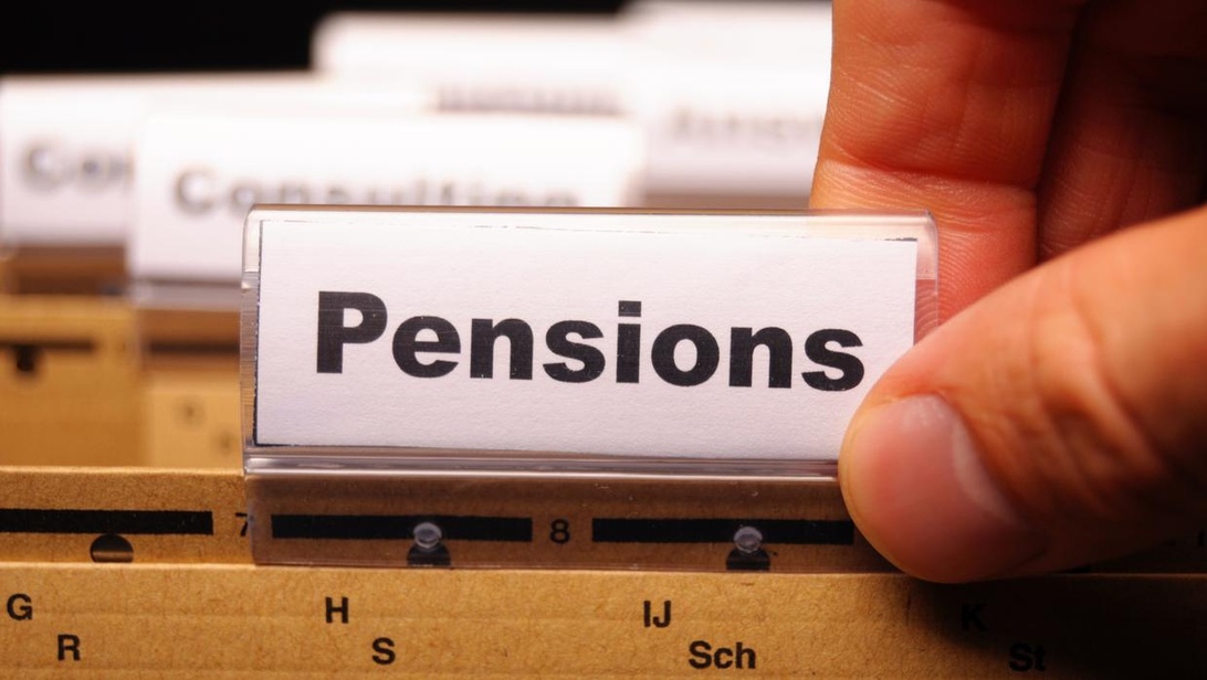 En närbild på en hand som håller i en registerflik märkt 'Pensioner' ovanför ett arkivsystem, vilket symboliserar en viktig del av seniorers ekonomiska planering.